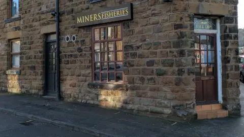 David Spereall/BBC The front of a fish-and-chip shop named 'Miners Fisheries'. It is an old-fashioned stone building with a brown door.
