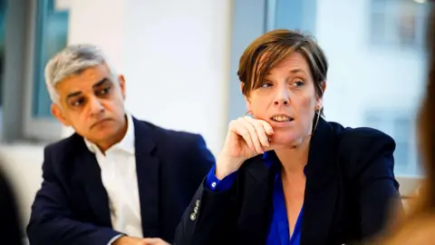 Minister for Safeguarding and Violence Against Women and Girls, Jess Phillips, and Mayor of London Sadiq Khan sit next to each other during a visit to Metropolitan Police's Croydon Custody Centre, in south London. They are both wearing navy blazers.