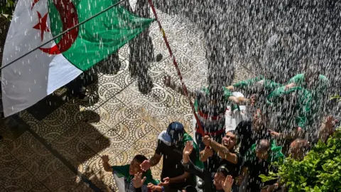 Getty Images Protesters wave the Algerian flag beneath a shower of water - Friday 10 May