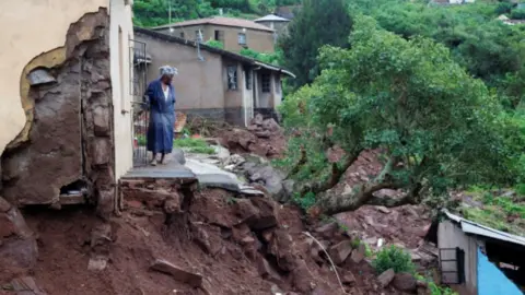 Reuters A woman stands at her front door after heavy rains caused flood damage in KwaNdengezi, Durban, South Africa - 12 April 2022