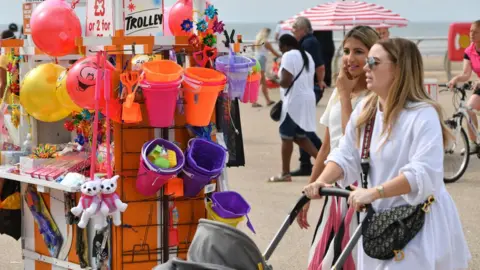 Getty Images Two women walk past a stall selling toys on a beach