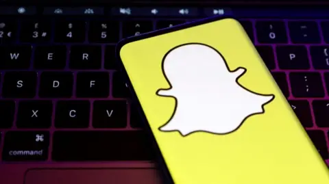 The white Snapchat logo is displayed against a bright yellow background on a mobile phone