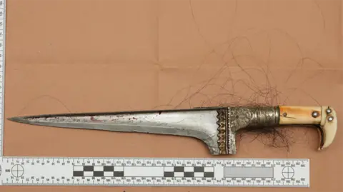 Crown Prosecution Service A silver-bladed dagger is pictured beside a ruler showing its length.
