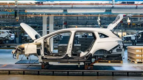 A white car half-built on the production line, with its boot and bonnet open