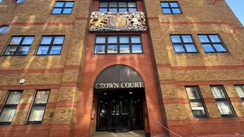 Julita Waleskiewicz/BBC St Albans Crown Court, view of the brown and orange brick building from the outside, with ''Crown Court'' written above the rotating black doors. 
