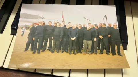 Grace Shaw/BBC/Filey Fisherman's Choir Group of 25 men in navy jumpers perform on Filey's Coble Landing