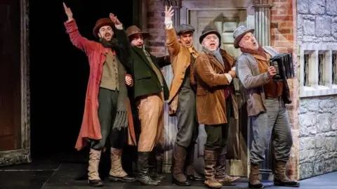 Paul Carr five ment singing and dressed in Victorian outfits and singing in front of a brick house.