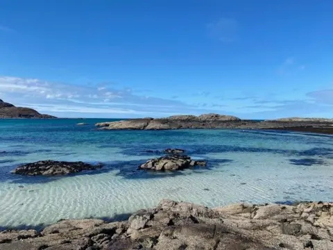 Steph Lamb A bay with crystal clear blue water and rocks.