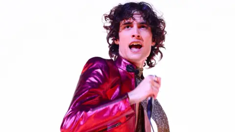 Getty Images Sombr, wearing a reflective pink jacket, performs against a stark white background at the 2026 Brit Awards ceremony