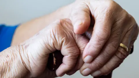 Two elderly hands clasping the top of a walking stick.