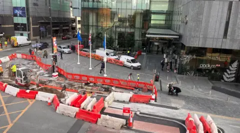 A wide shot of the roadworks in Deansgate. Construction fences are lined up to make large areas of a road inaccessible.