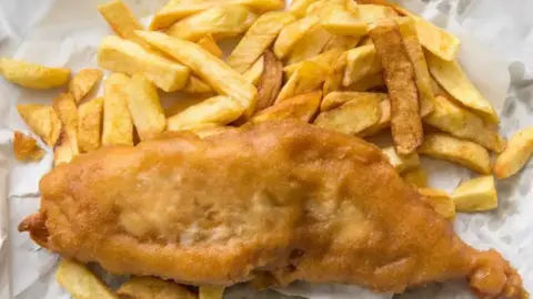 A stock image of fish and chips on white paper.