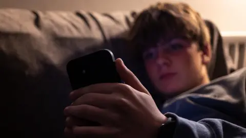 Getty Images Young boy looks at his phone on a sofa