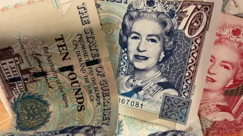 Three different notes of Guernsey currency. The feature a portrait of Queen Elizabeth II and the words THE STES OF GUERNSEY along with their denomination TEN POUNDS £10.