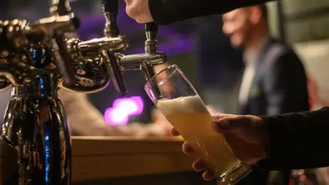 Getty Images A pint being pulled in a pub. A man can be seen out of focus in the background.