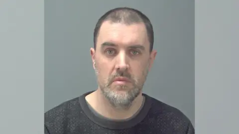 Suffolk Police A police custody mugshot of Martin Woods - a man with shaven black hair and grey/white facial hair