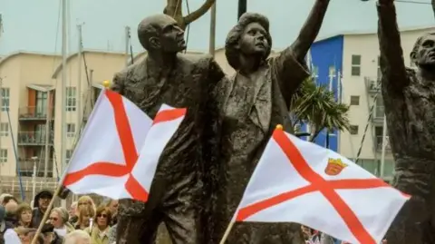 BBC A bronze statue of a man and woman with two Jersey flags in the foreground. 
