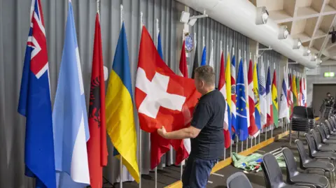 EPA Row of flags on display at the conference, with people pulling the Swiss flag