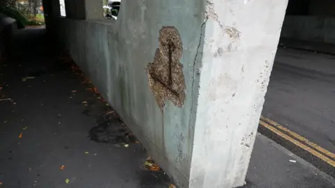 A close up of one of the bridge supports, with a chuck of concrete missing from its side.