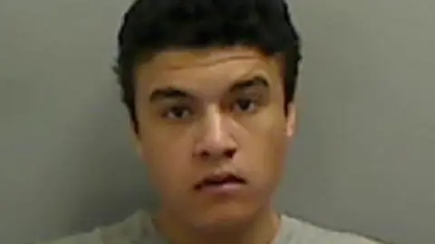 Mugshot of Cartel Collinson, who has short black hair and thick black eyebrows. He is wearing a grey jumper. 