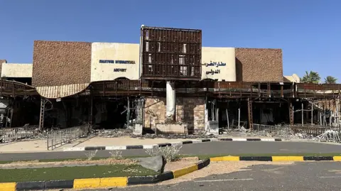 Anadolu via Getty Images A view of the damage caused by clashes between the Sudanese army and the Rapid Support Forces. The entrance to the airport terminal is partly destroyed.