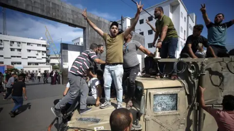 EPA Palestinian stand on a captured Israeli jeep on a street in Gaza (7 October 2023)