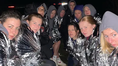 Andy Harper A group of women huddled together in silver fire blankets at the side of the road