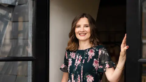 Petra Gatto Sleep counsellor Kat Lederle wears a black dress with pink flowers and has shoulder length brown hair.