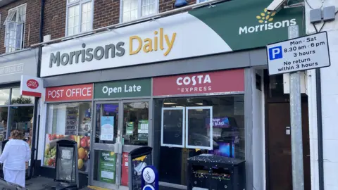A Morrisons Daily Post Office on Burpham high street with signs saying "Open Late" and "Costa Express"