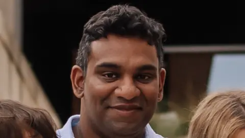Gihan Ganesh, wearing an open-necked blue shirt, looks straight into the camera.
