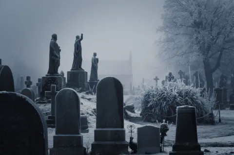 Brian Colston Cemetery with older style headstones in varying shapes on a foggy day with ice covering the tree's, bushes and grass