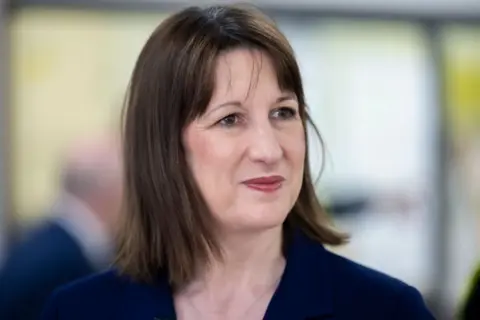 Getty Images Chancellor Rachel Reeves smiles on a visit to Bury, in the northwest of England. She is wearing a navy blue suit.