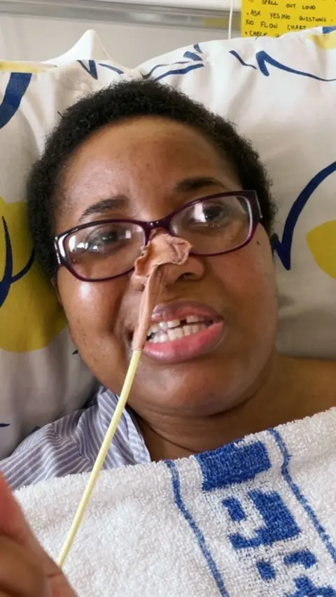 A woman lying on a hospital bed with a tube coming out of her nose