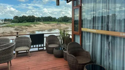 Jonathan Head/BBC A view of the villa that is being used by He Yingxiong who is currently running Shwe Kokko. A decking area with woven chairs overlooks a river and green trees on the other side