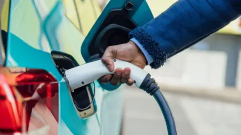 A side view close up shot of an unrecognisable mid adult businessman wearing formal businesswear putting his electric car on charge at a public charging point .