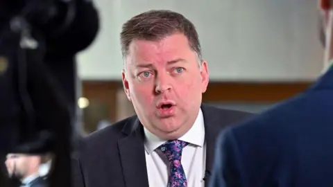 Getty Images Colin Smyth, a man with spiky brown hair mid speech while wearing a suit, white shirt and blue flowery tie