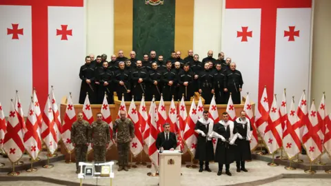 AFP via Getty Images Mikheil Kavelashvili speaking in parliament at is inauguration ceremony, where he is standing in front of Georgian flags and a group of officers with guns