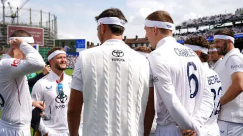 PA Media England team before take the field on 'A Day for Thorpey' in memory of England and Surrey cricketer Graham Thorpe on what would have been his 56th birthday on day two of the Fifth Rothesay Men's Test at the Kia Oval, London. They are all wearing cricket whites and have white headbands on.