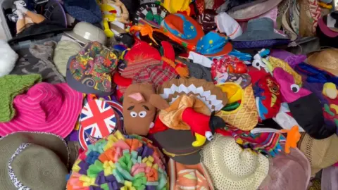 Image of a surface completely covered by a variety of hats of all colours and variations including characters like Scooby Doo, in addition to regular sunhats.