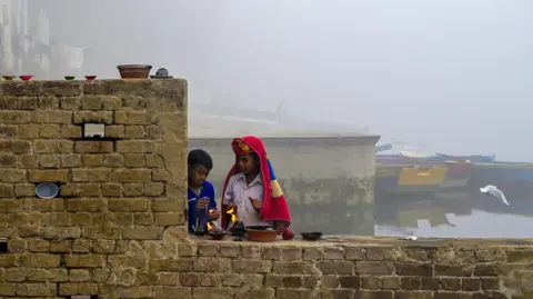 Getty Images Boys light lamps on a brick wall on a bank of the river Yamuna in Delhi. Smog engulfs their surroundings