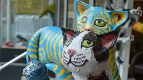 Will Hebditch Three colourful papier-mâché models of cats. 