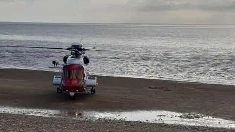 Caroline Robb A coastguard helicopter on a beach with what looks like a calm sea in the background.