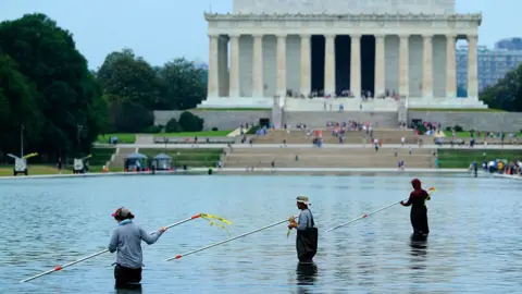 Workers with long poles clean the pool with the Lincoln Monument in the background