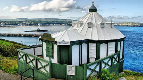 MANX SCENES A view of the Camera Obscura, a white and green small round building, you can see the sea in the background along with the Tower of Refuge and Douglas Promenade.