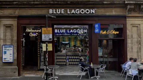 A google view of the front of the Blue Lagoon chi shop with four people sitting at tables on the street outside