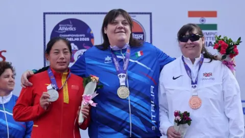 Reuters/Bhawika Chhabra Três mulheres estão em um pódio. A Assunta Legnante (centro) do metal dourado com a medalha de prata Zhao sim (esquerda) e a medalha de bronze de Lydia, Grã -Bretanha (direita). Use o topo da pena e tenha suas medalhas ao redor de suas gargantas e todo mundo tem um pacote de flores