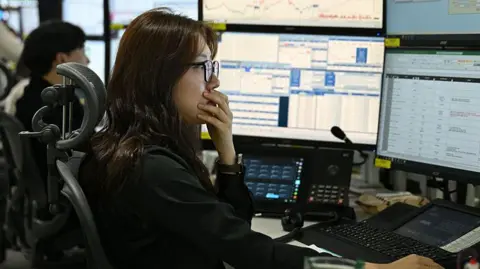 A currency dealer has her hand over her mouth as she and her team monitor exchange rates in a dealing room at the Hana Bank headquarters in Seoul on 4 March 