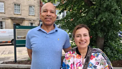 Local Democracy Reporting Service Charles and Daniella McKinney standing in Sleaford town centre smiling at the camera. Charles is bald and is wearing a light blue polo T-shirt. Daniella has brown hair tied back and is wearing a colourful patterned jacket.