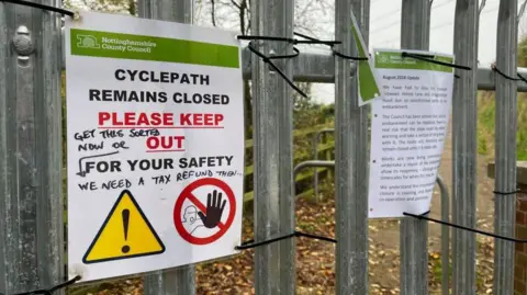 A laminated sign warning people that a cycle path is closed, telling people to 'PLEASE KEEP OUT'.