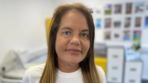 Becky Joyce, with long brown hair and wearing a white T-shirt, looks at the camera.